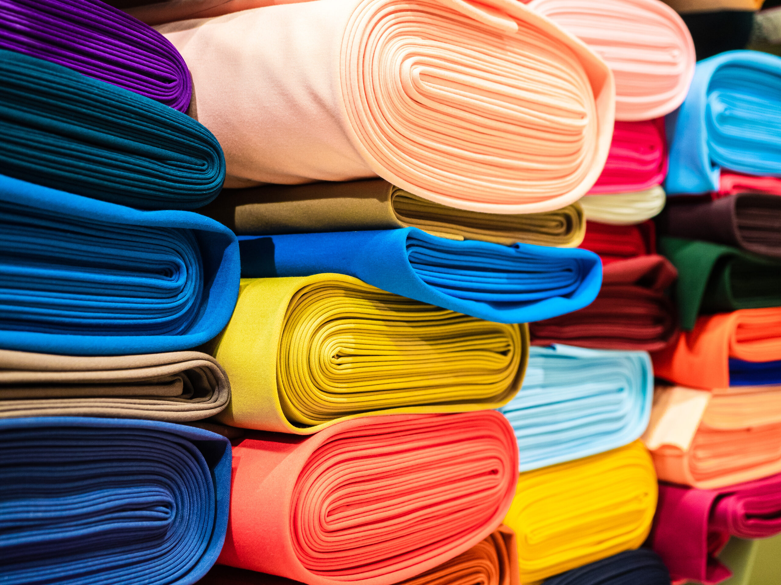 Rolls of bright multicolored fabric close-up. Coils of fabric are on the shelves in the store. Sample of coat cotton fabric in rolls Textile-clothing